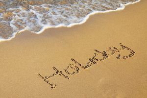 Billede af en sand strand, hvor der er skrevet teksten Holiday i sandet.